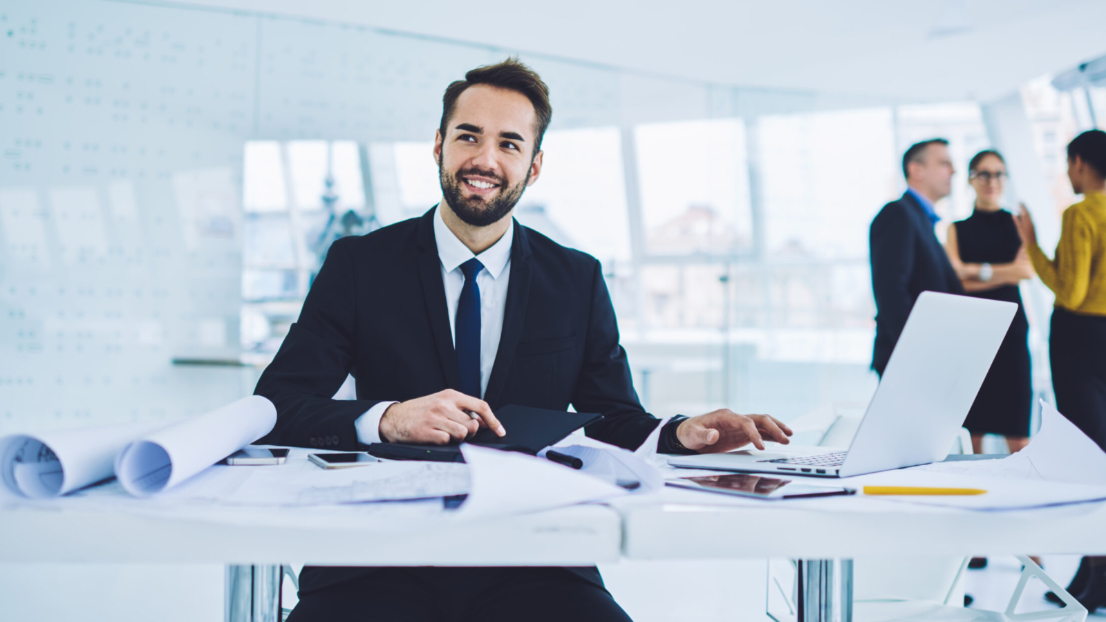 Successful male entrepreneur in formal clothing enjoying work time for developing startup project, happy businessman analyzing productive strategy sitting at table desktop in office interior