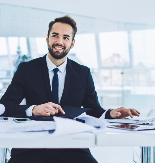Successful male entrepreneur in formal clothing enjoying work time for developing startup project, happy businessman analyzing productive strategy sitting at table desktop in office interior
