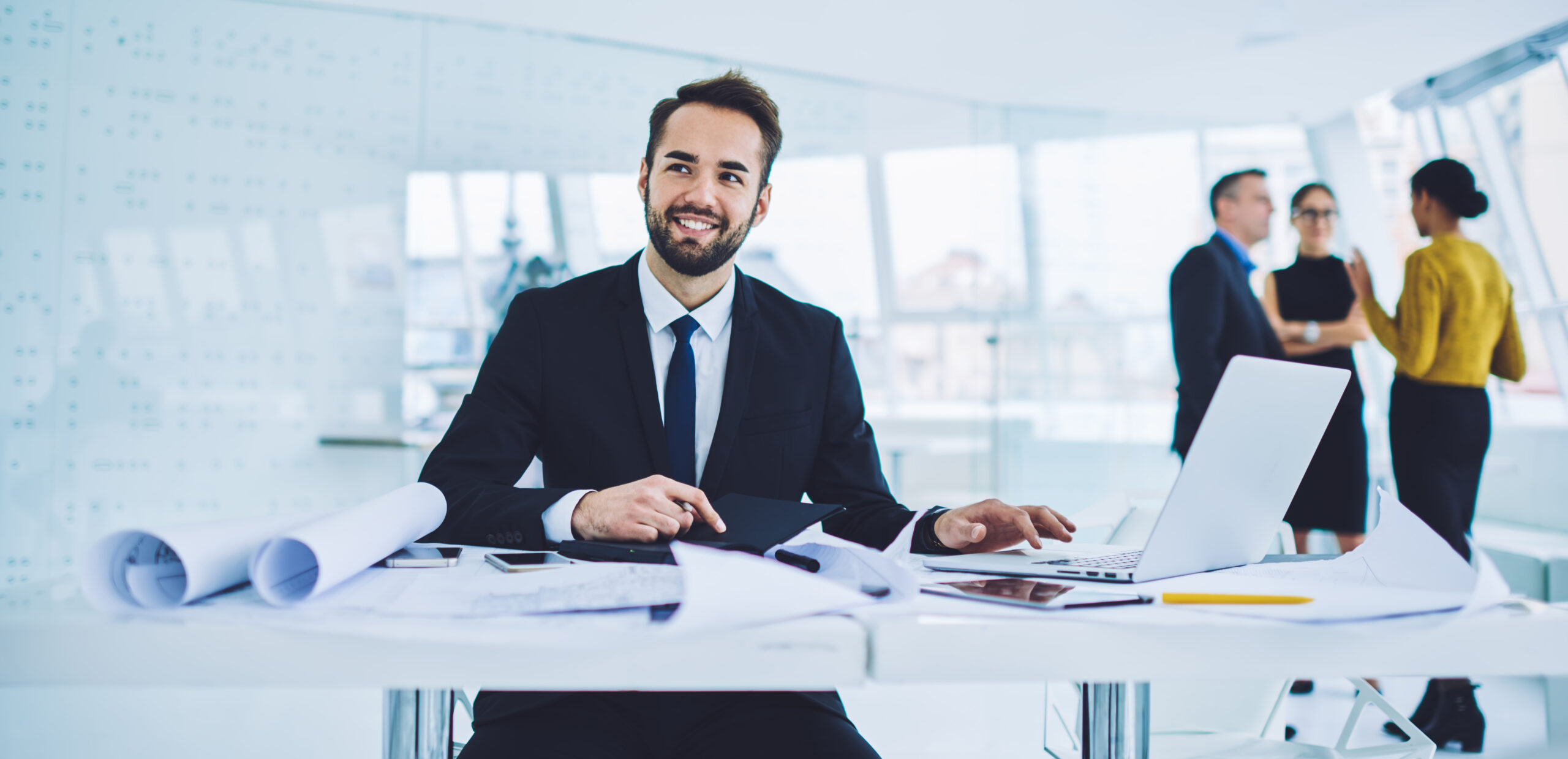 Successful male entrepreneur in formal clothing enjoying work time for developing startup project, happy businessman analyzing productive strategy sitting at table desktop in office interior