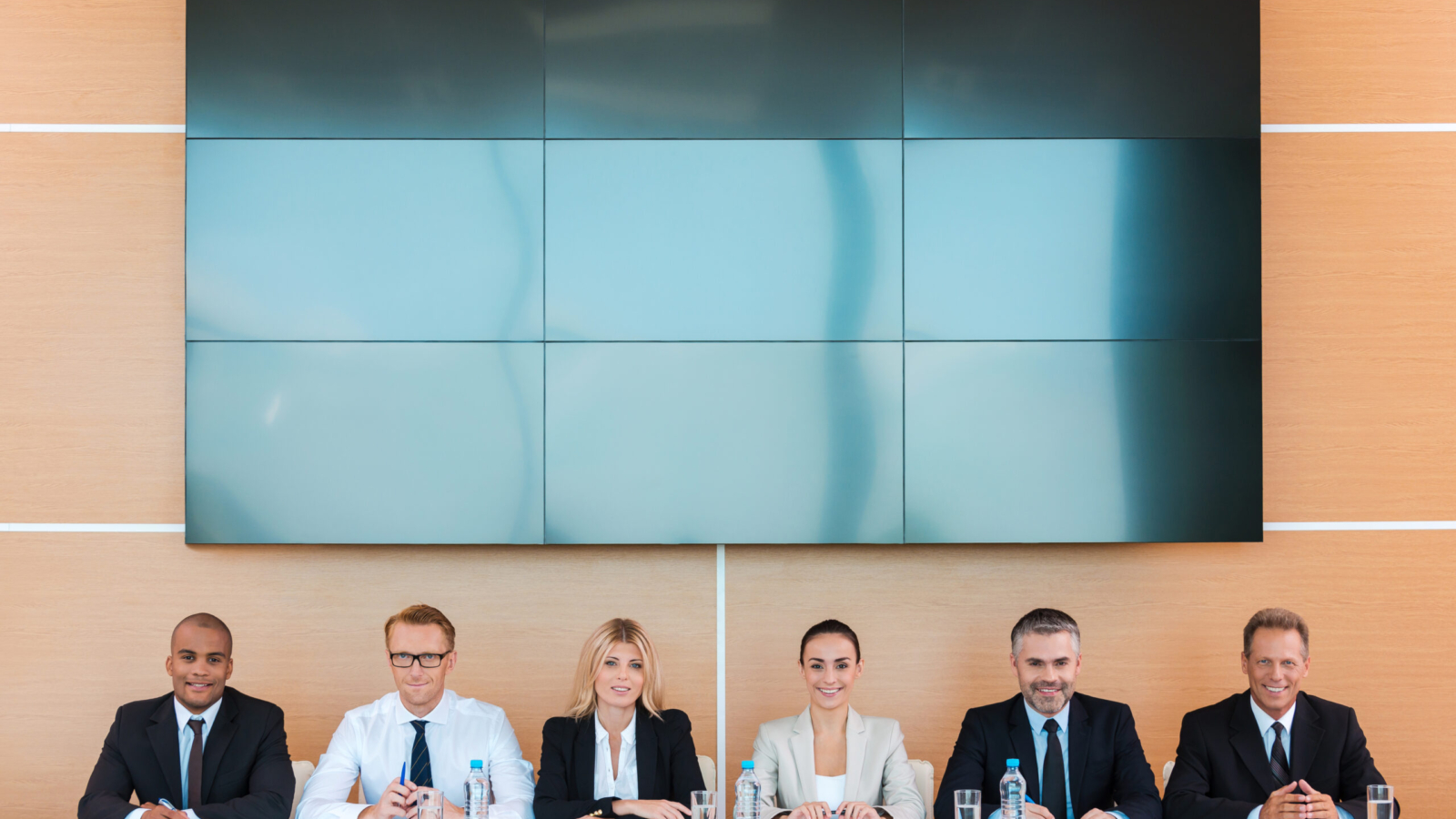 Confident business team. Group of business people sitting together at the table and smiling with large monitor upon their heads
